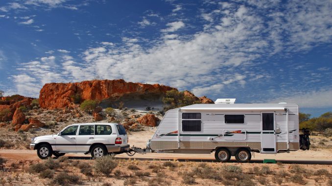 Four wheel drive and offroad caravan in outback Australia against a stunning red rock outcrop with an deep blue sky and interesting cloud formations