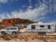 Four wheel drive and offroad caravan in outback Australia against a stunning red rock outcrop with an deep blue sky and interesting cloud formations