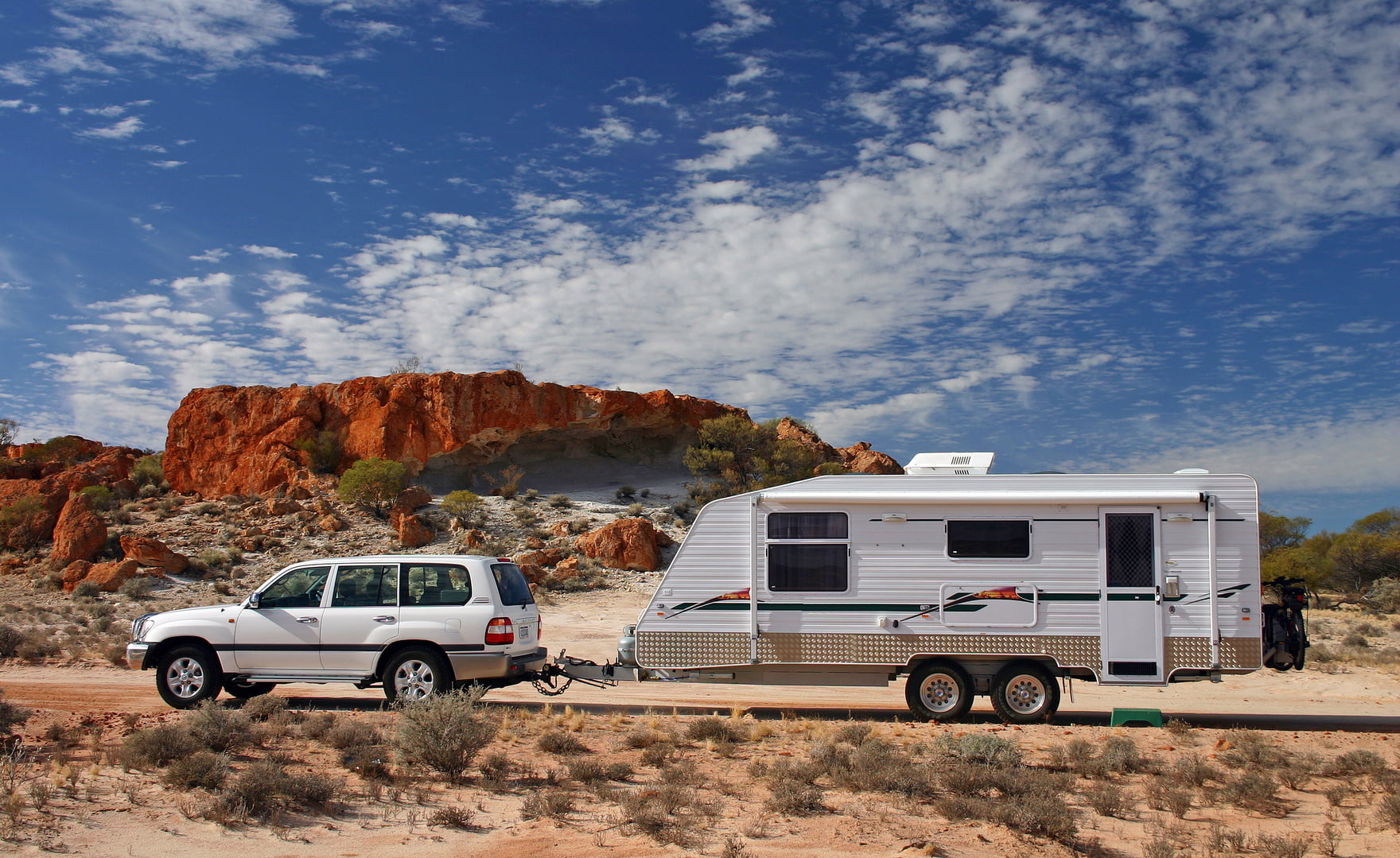 Four wheel drive and offroad caravan in outback Australia against a stunning red rock outcrop with an deep blue sky and interesting cloud formations