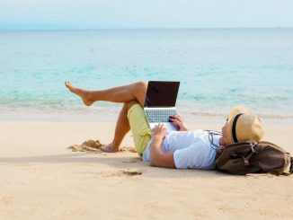 man sitting on beach with laptop